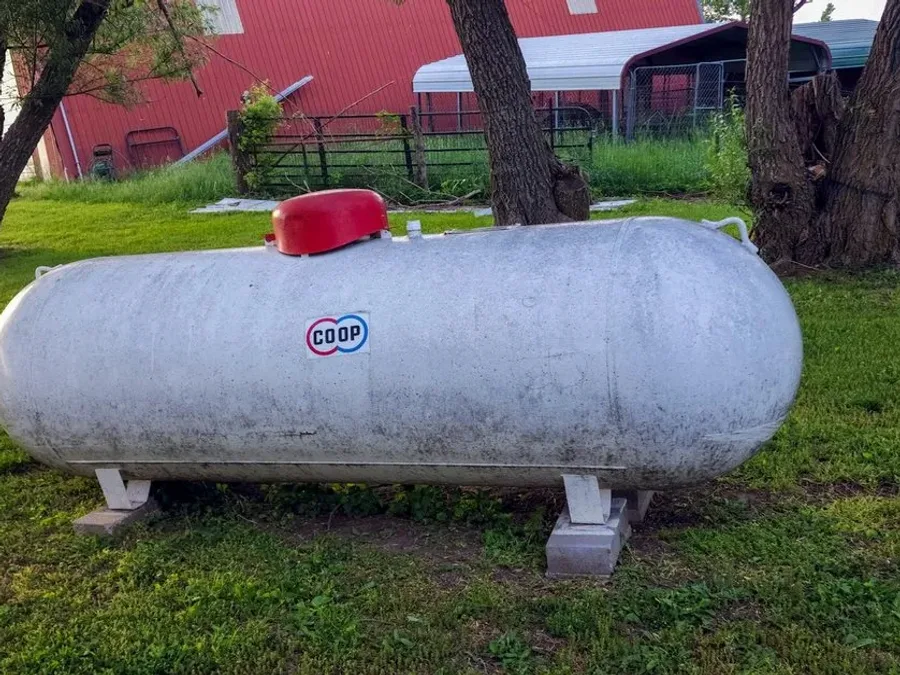 Propane tank on a lawn beside a red barn